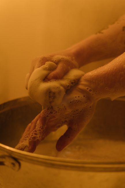 A close-up of a person’s hands covered in soap suds, washing a cardboard box inside a home. The hands are positioned over the box, which is situated on a surface, with foam and bubbles visible around the fingers. The background features warm lighting and a plain wall, indicating an indoor setting. This cleaning activity may be part of packing or preparing items for a home relocation, related to furniture transport and packing during a house removal. The image illustrates the careful handling involved in moving and packing tasks, which are key components of professional removals services offered by Man with Van Wormwood Scrubs.