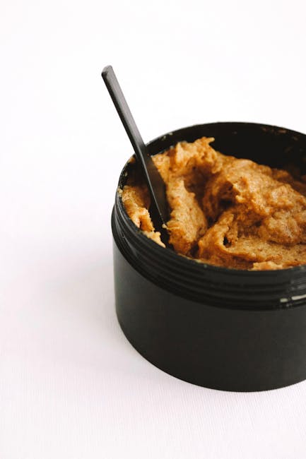 A round, black plastic container filled with a brown, textured substance, likely a spread or paste, with a small metal spoon partially submerged into it. The container is placed on a plain white surface, highlighting the contrast between the dark container and the light background. The image focuses on the food item and utensil, with no additional objects or environment visible, suitable for illustrating food packaging or prepared ingredients in a home or kitchen setting. This detailed description supports accessibility and visually accurate representation for content related to moving or packing food items during a house removal process, as seen on the Wormwood Scrubs moving guide page by Man with Van Wormwood Scrubs.